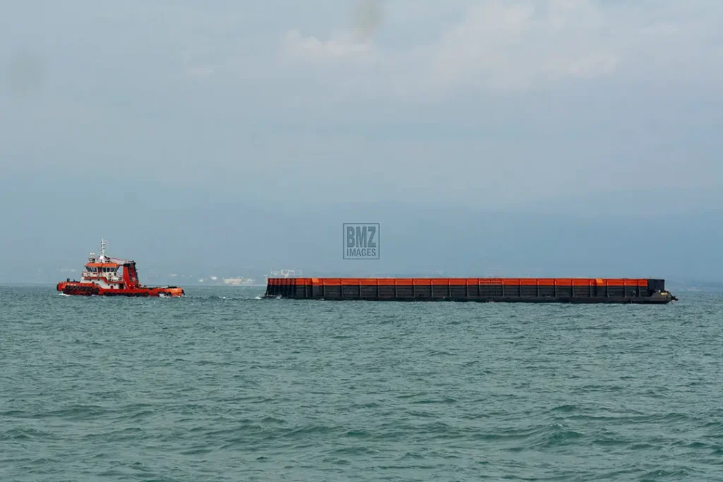 Sebuah tug boat menarik kapal tongkang bermuatan material galian C untuk pembangunan Ibu Kota Nusantara (IKN) di pesisir Teluk Palu, Sulawesi Tengah, Kamis (12/6/2025). Data dari Minerba One Map Indonesia (MOMI) Kementerian ESDM, sekitar 30 juta ton batu pecah dipasok dari usaha pertambangan di Sulawesi Tengah untuk pembangunan IKN dan hingga akhir 2024 tercatat 69 izin pertambangan galian C aktif di Kota Palu dan Donggala dengan total luas lahan 1.764,41 hektare. (bmzIMAGES/Basri Marzuki)